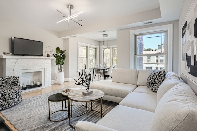 living room with wood-type flooring, a fireplace, a chandelier, and a wealth of natural light