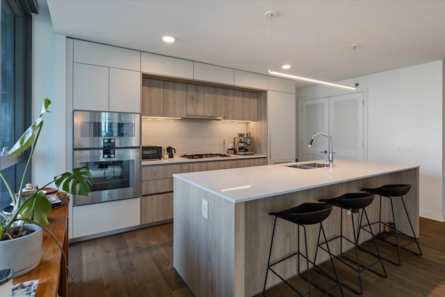 kitchen featuring stainless steel appliances, a kitchen island with sink, sink, and dark hardwood / wood-style flooring