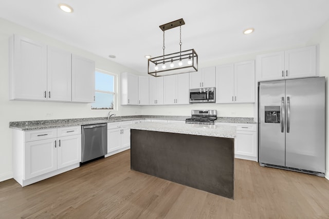 kitchen with light wood-type flooring, stainless steel appliances, a center island, hanging light fixtures, and white cabinets