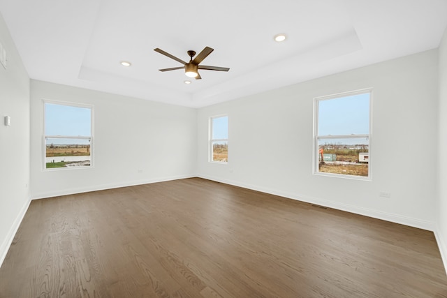 empty room with a tray ceiling, ceiling fan, and dark hardwood / wood-style flooring