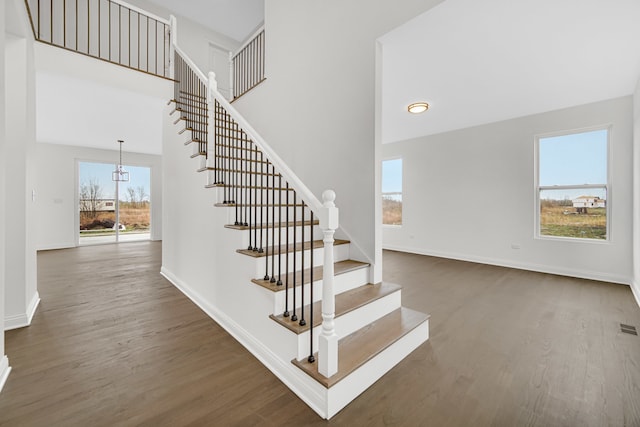 stairway with a towering ceiling, hardwood / wood-style floors, and a notable chandelier