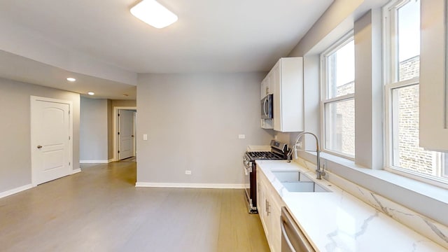 kitchen with white cabinets, appliances with stainless steel finishes, plenty of natural light, and light hardwood / wood-style flooring