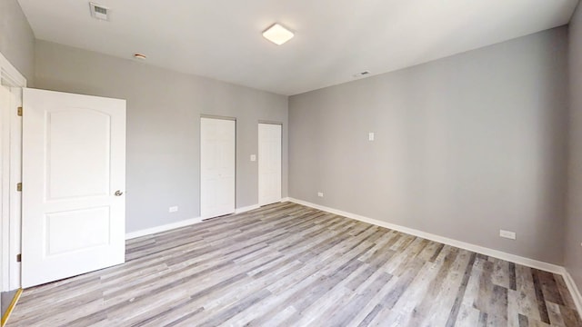 unfurnished bedroom featuring multiple closets and light hardwood / wood-style flooring