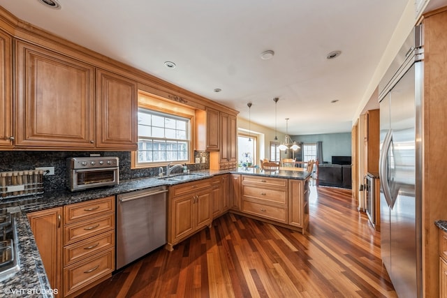 kitchen with hanging light fixtures, sink, decorative backsplash, dark wood-type flooring, and appliances with stainless steel finishes