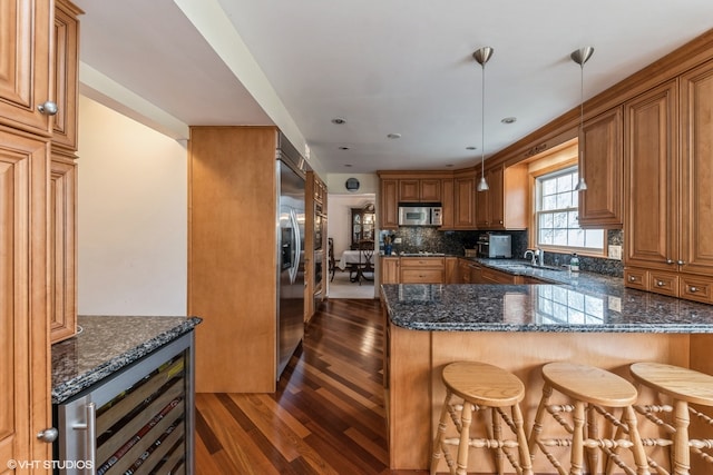 kitchen with hanging light fixtures, dark stone countertops, appliances with stainless steel finishes, dark hardwood / wood-style floors, and kitchen peninsula