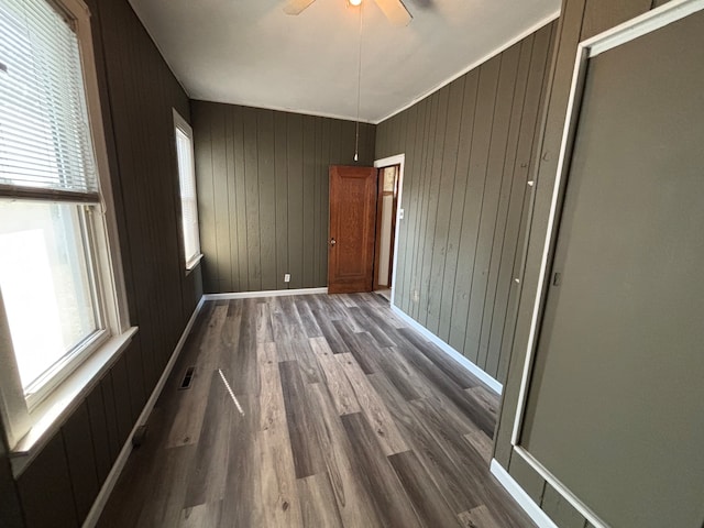 unfurnished room featuring dark wood-type flooring, ceiling fan, and wood walls