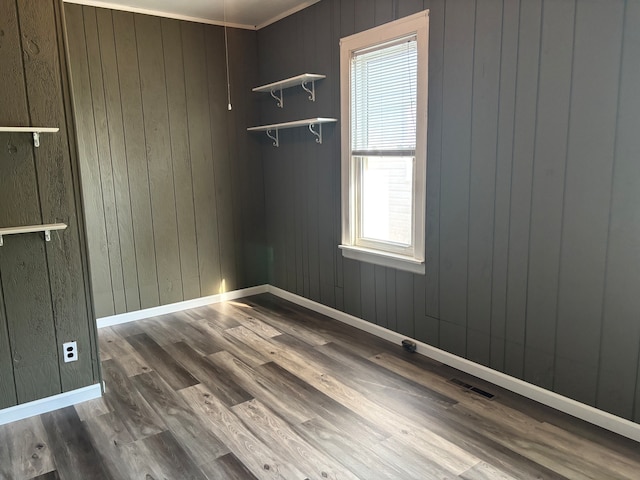 empty room with crown molding, wood walls, and hardwood / wood-style flooring