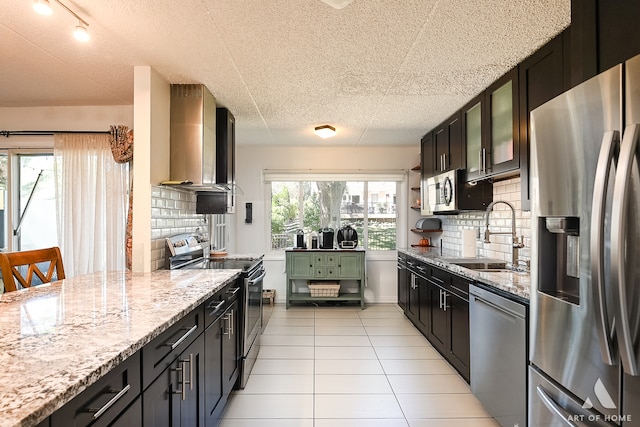 kitchen featuring backsplash, stainless steel appliances, sink, light stone countertops, and wall chimney exhaust hood