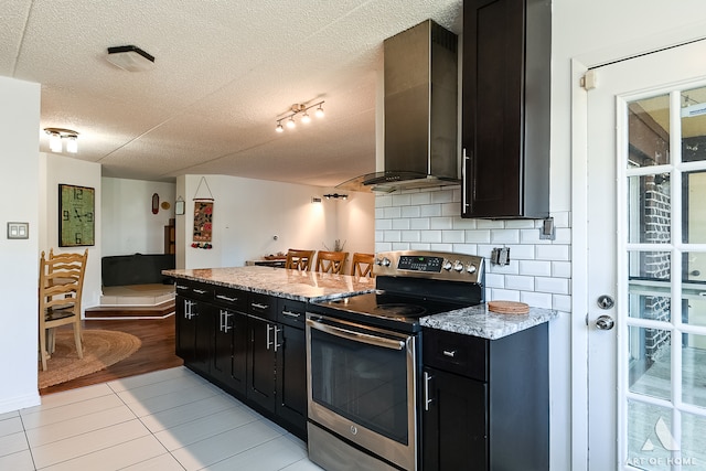 kitchen with a textured ceiling, stainless steel electric range oven, decorative backsplash, light stone counters, and wall chimney range hood