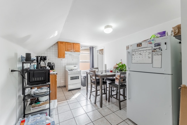 kitchen featuring light tile patterned floors, white appliances, lofted ceiling, tile walls, and light brown cabinets