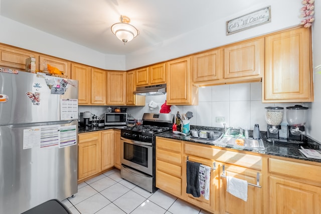 kitchen featuring light brown cabinetry, light tile patterned floors, appliances with stainless steel finishes, tasteful backsplash, and dark stone counters