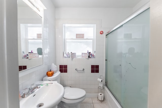 full bathroom featuring toilet, tile patterned floors, sink, bath / shower combo with glass door, and tile walls