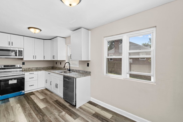 kitchen with light stone countertops, appliances with stainless steel finishes, dark wood-type flooring, sink, and white cabinetry