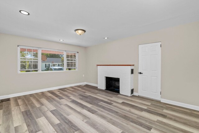 unfurnished living room featuring a brick fireplace and light hardwood / wood-style floors