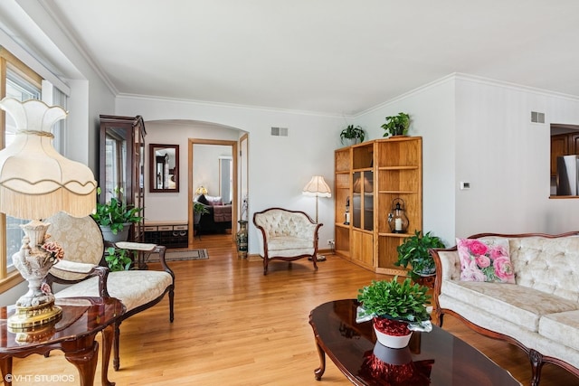 living area featuring arched walkways, light wood-type flooring, crown molding, and baseboards
