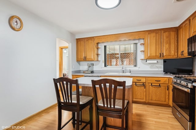 kitchen with gas stove, a sink, open shelves, light wood-type flooring, and arched walkways