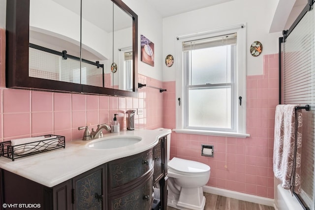 full bathroom with tile walls, plenty of natural light, toilet, vanity, and wood finished floors