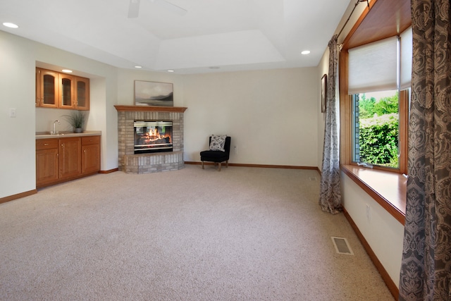 carpeted living room featuring ceiling fan, sink, a fireplace, and a raised ceiling