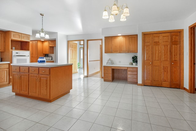 kitchen with pendant lighting, built in desk, a notable chandelier, a kitchen island, and oven