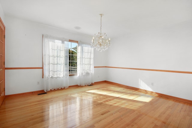 unfurnished room featuring a notable chandelier and light hardwood / wood-style floors