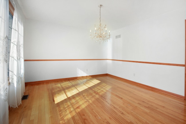 empty room with an inviting chandelier and light hardwood / wood-style flooring