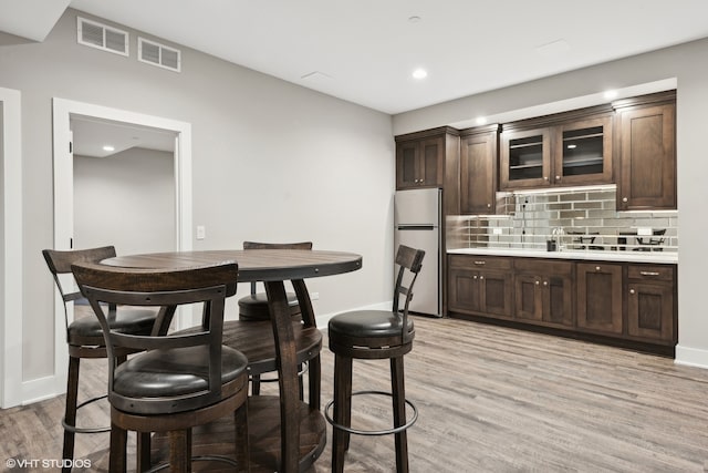 kitchen featuring light hardwood / wood-style flooring, dark brown cabinets, backsplash, and white fridge