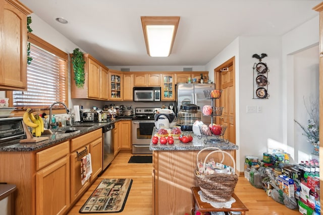 kitchen featuring stainless steel appliances, light hardwood / wood-style floors, dark stone counters, and sink