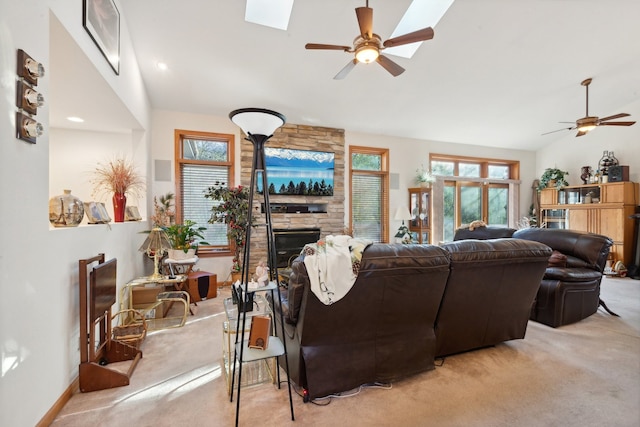 carpeted living room featuring vaulted ceiling with skylight, ceiling fan, and a fireplace