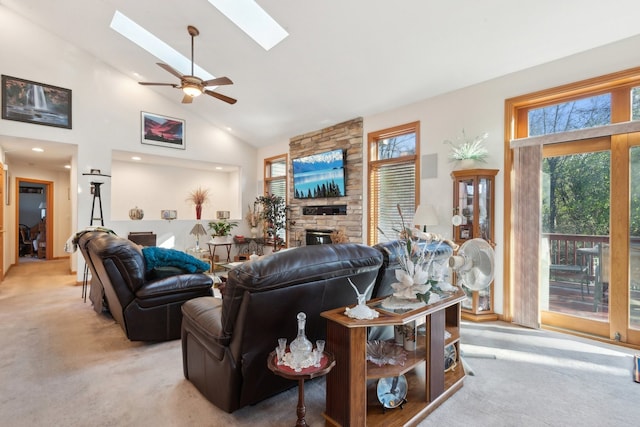 living room with a fireplace, high vaulted ceiling, a skylight, light colored carpet, and ceiling fan