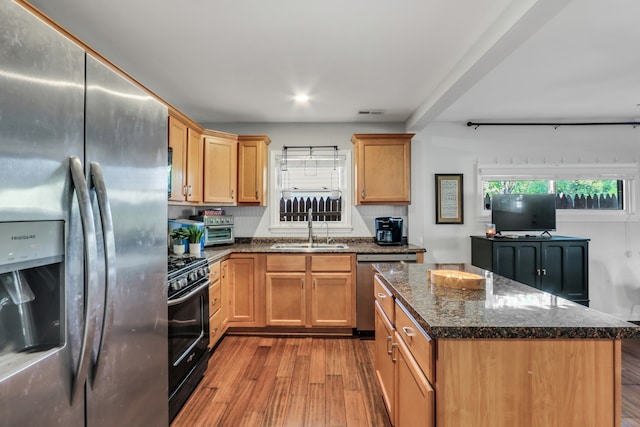 kitchen featuring light hardwood / wood-style flooring, appliances with stainless steel finishes, a center island, sink, and dark stone counters