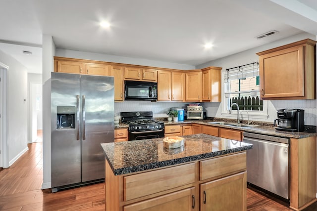 kitchen with hardwood / wood-style floors, sink, black appliances, dark stone counters, and a kitchen island