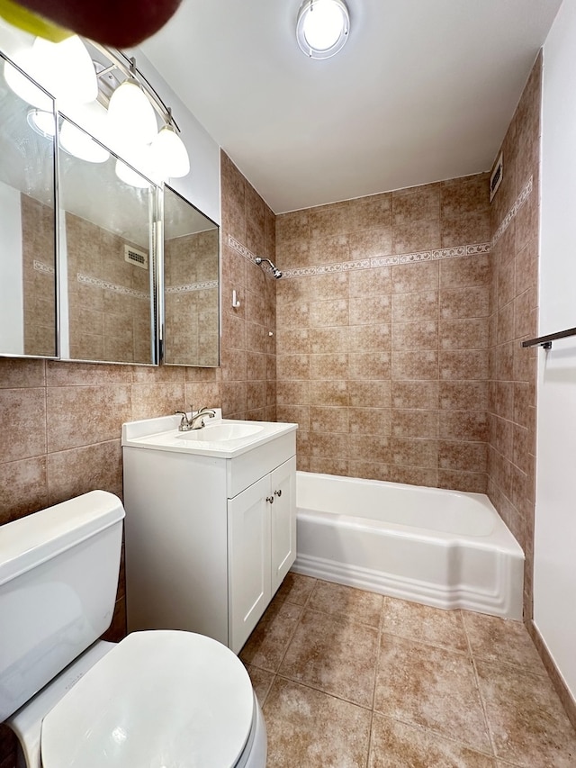 full bathroom with toilet, tile patterned floors, tiled shower / bath, vanity, and tile walls