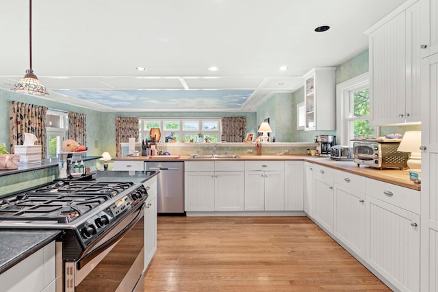 kitchen featuring white cabinets, stainless steel appliances, light wood-type flooring, and pendant lighting