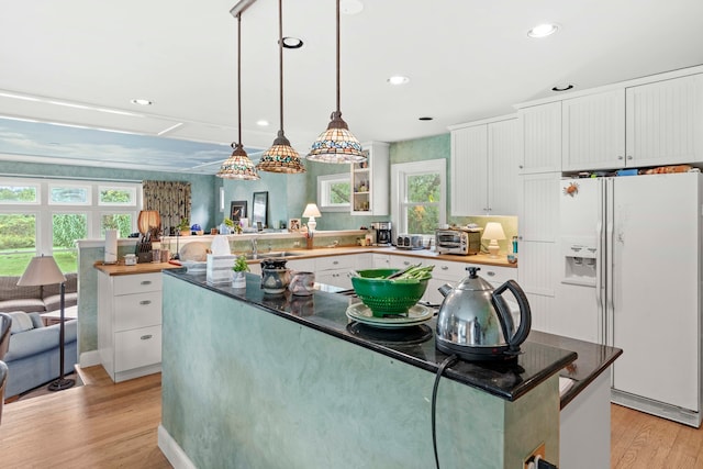 kitchen with white fridge with ice dispenser, plenty of natural light, white cabinets, and light wood-type flooring