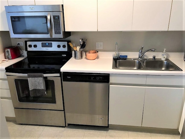 kitchen with appliances with stainless steel finishes, white cabinetry, sink, and light tile patterned flooring