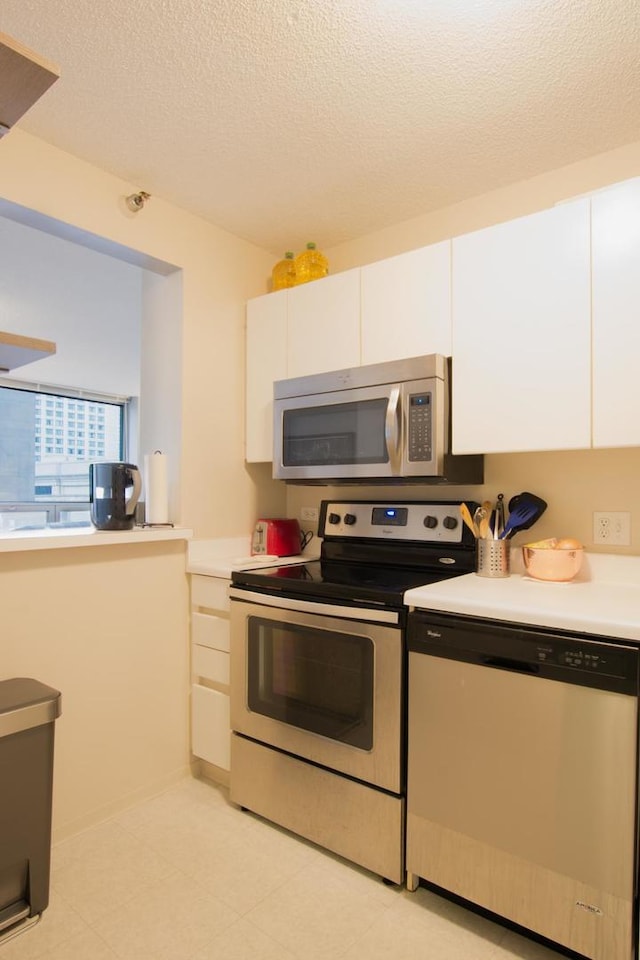 kitchen with a textured ceiling, appliances with stainless steel finishes, and white cabinetry