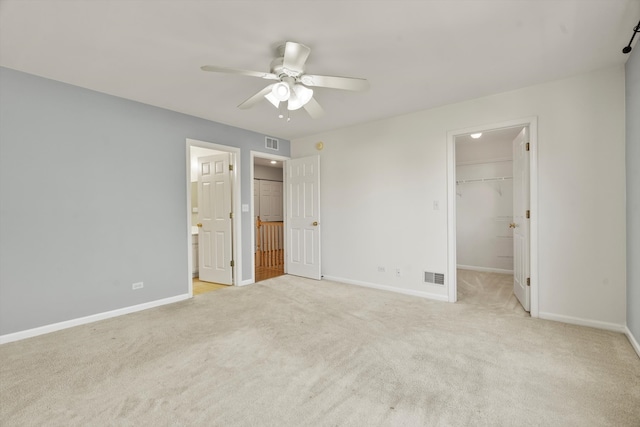 unfurnished bedroom with light carpet, a closet, a spacious closet, ceiling fan, and connected bathroom