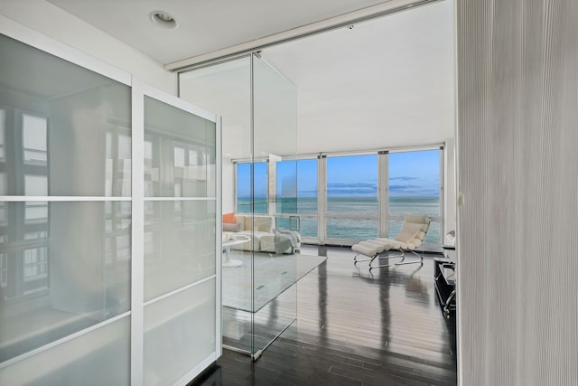 interior space with dark wood-type flooring, a wall of windows, and a water view