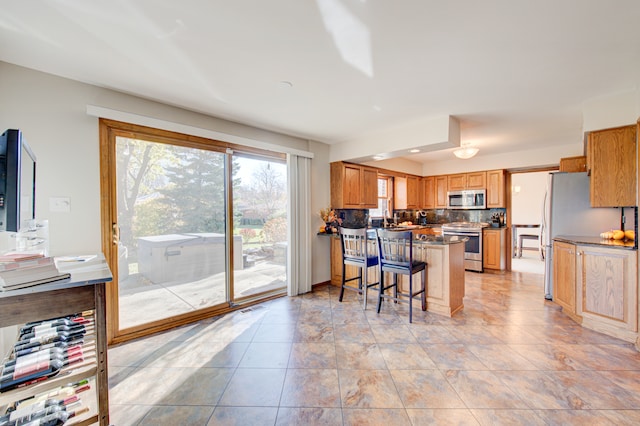 kitchen with appliances with stainless steel finishes, light tile patterned floors, a kitchen breakfast bar, and decorative backsplash