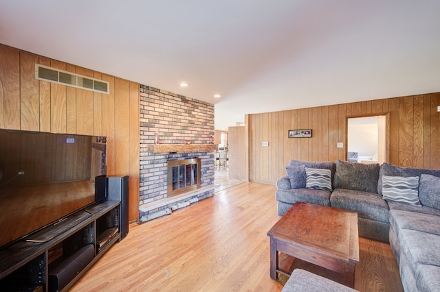 living room with light hardwood / wood-style flooring, a brick fireplace, and wooden walls