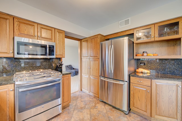 kitchen with dark stone countertops, stainless steel appliances, and backsplash