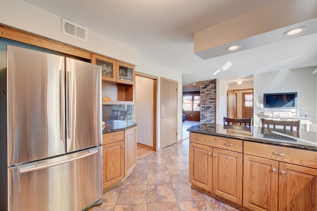 kitchen featuring dark stone counters, light tile patterned floors, and stainless steel refrigerator