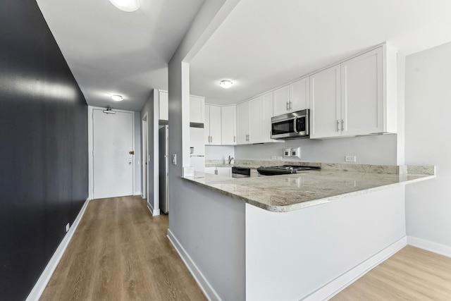 kitchen with light hardwood / wood-style floors, kitchen peninsula, light stone countertops, appliances with stainless steel finishes, and white cabinets