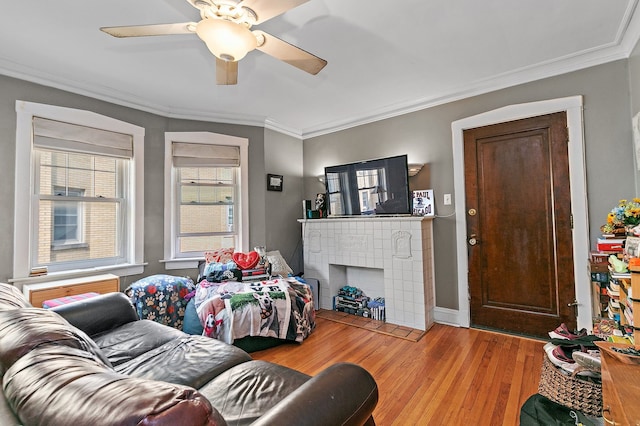 living room with crown molding, a tiled fireplace, ceiling fan, and light hardwood / wood-style floors