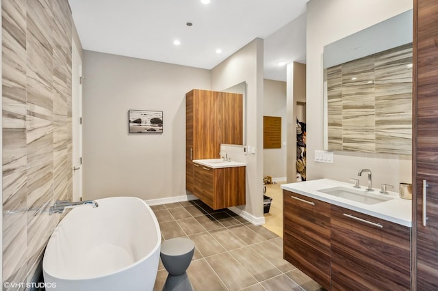 full bath featuring two vanities, a freestanding tub, tile patterned flooring, baseboards, and recessed lighting