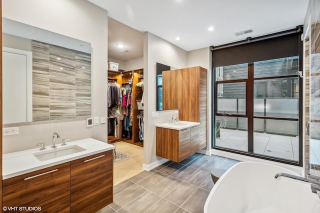 full bathroom with two vanities, tile patterned flooring, a freestanding tub, a walk in closet, and recessed lighting