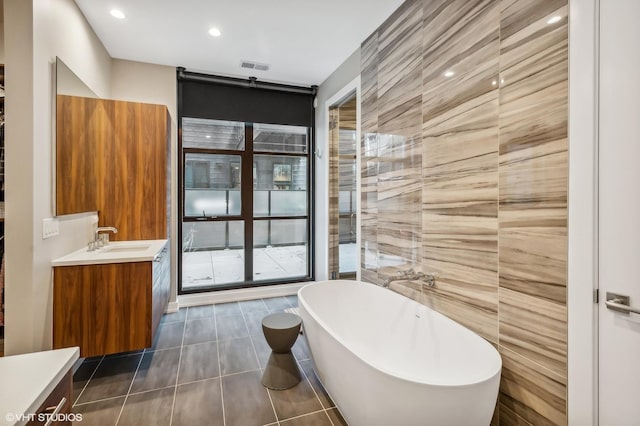 bathroom featuring vanity, a freestanding tub, tile patterned floors, recessed lighting, and tile walls