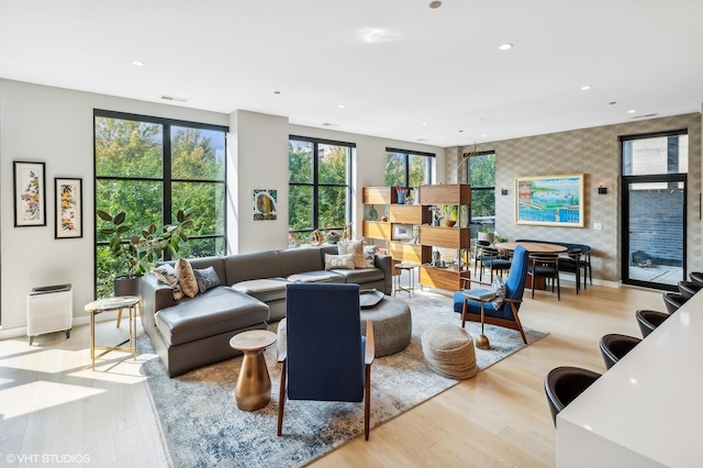 living area with wallpapered walls, an accent wall, light wood-type flooring, baseboards, and recessed lighting