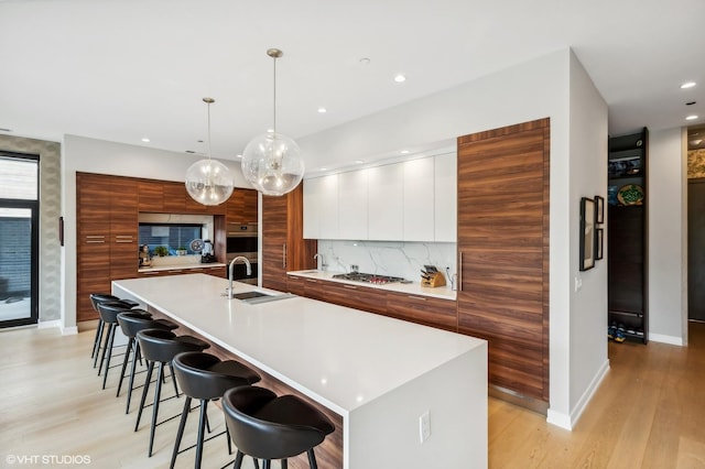kitchen with modern cabinets, a sink, light wood-type flooring, baseboards, and recessed lighting