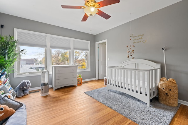 bedroom featuring a crib, wood-type flooring, and ceiling fan